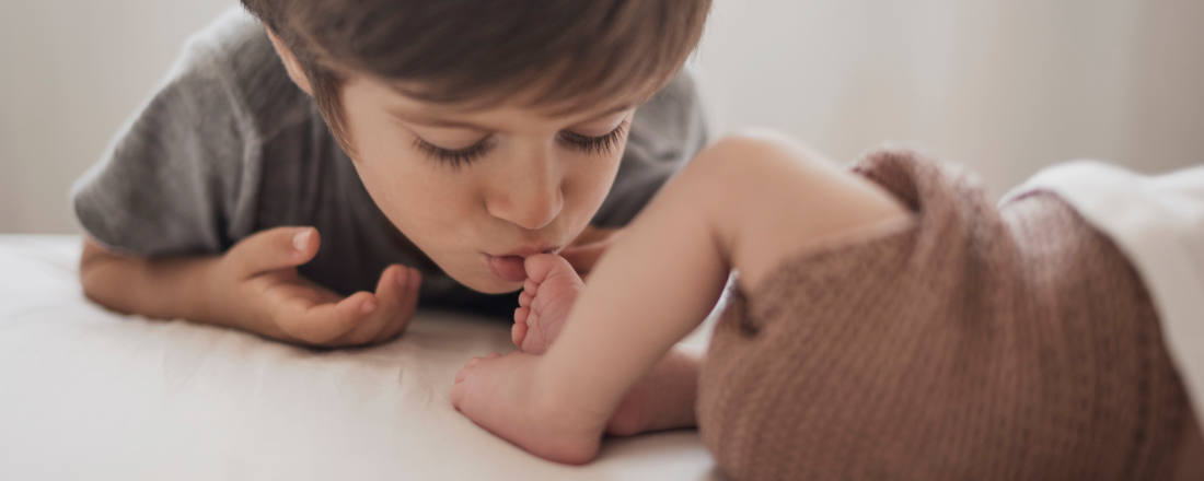 Image-du-Blog-ruedeloeuvre-represente-un-grand-frere-qui embrasse-le-petit-pied-de-son-petit-frere-pour-larticle-Les-meilleurs-moments-pour-photographier-un-nouveau-ne